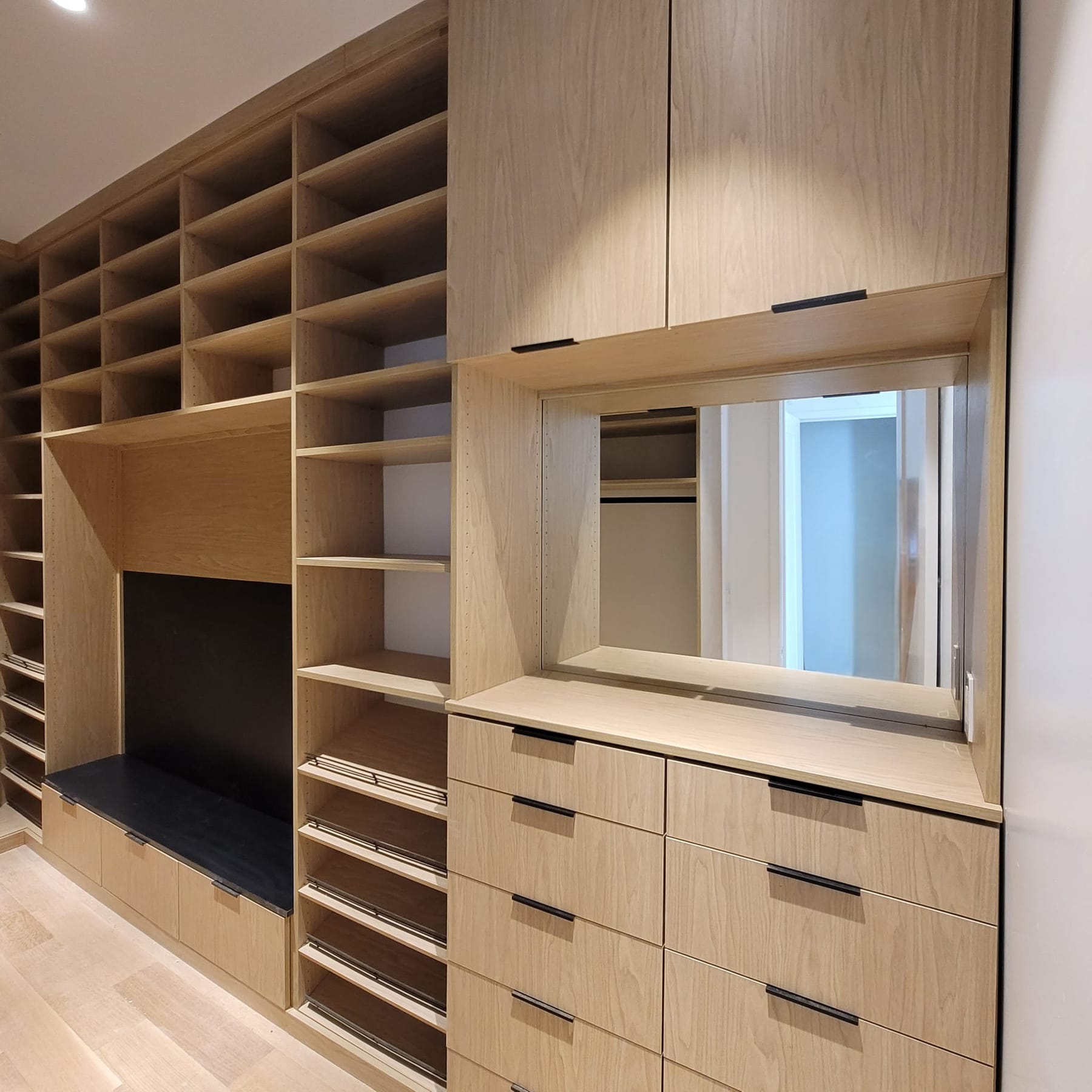 A full wall of light oak shelving, drawers and a mirrored opening