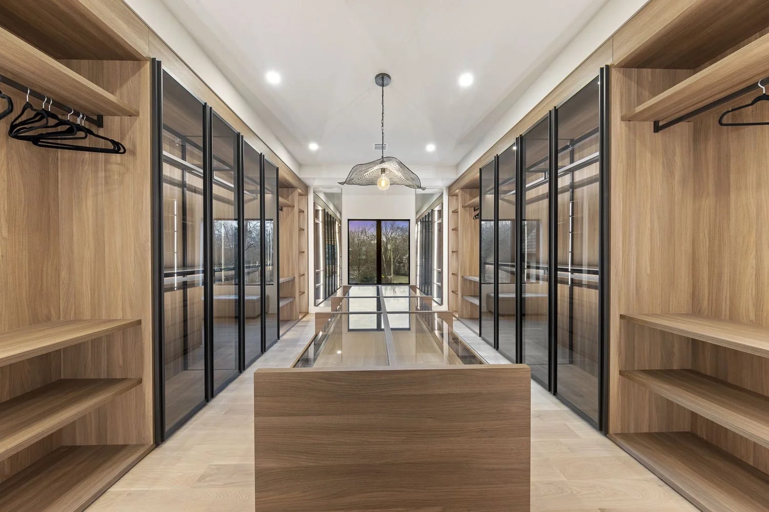 A long dressing room with glass-fronted wardrobes down both sides and an island running the length of it